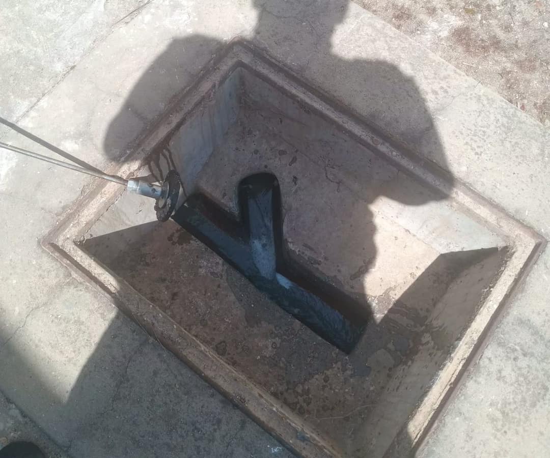 Drain rods with a scraper disc going into an open concrete inspection chamber, water running through the channel at the bottom