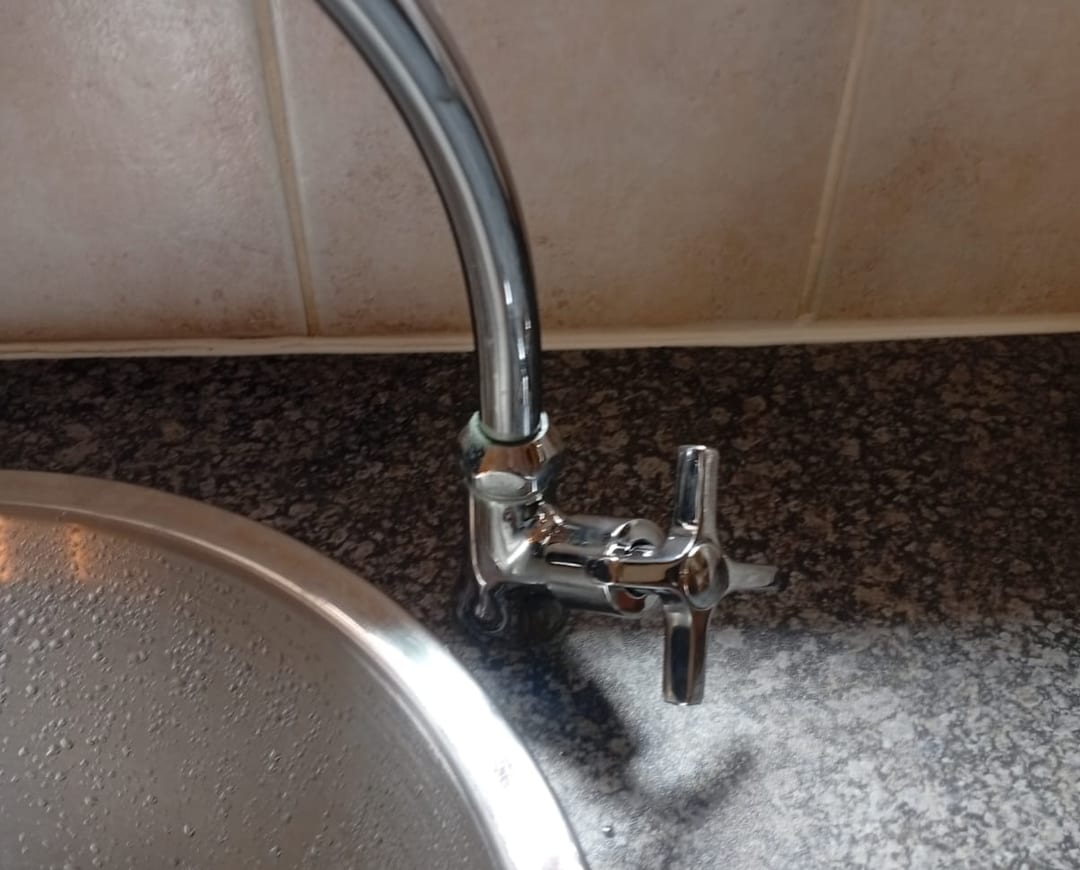 Chrome swan-neck kitchen tap with a cross-head handle beside a stainless steel sink on a granite worktop